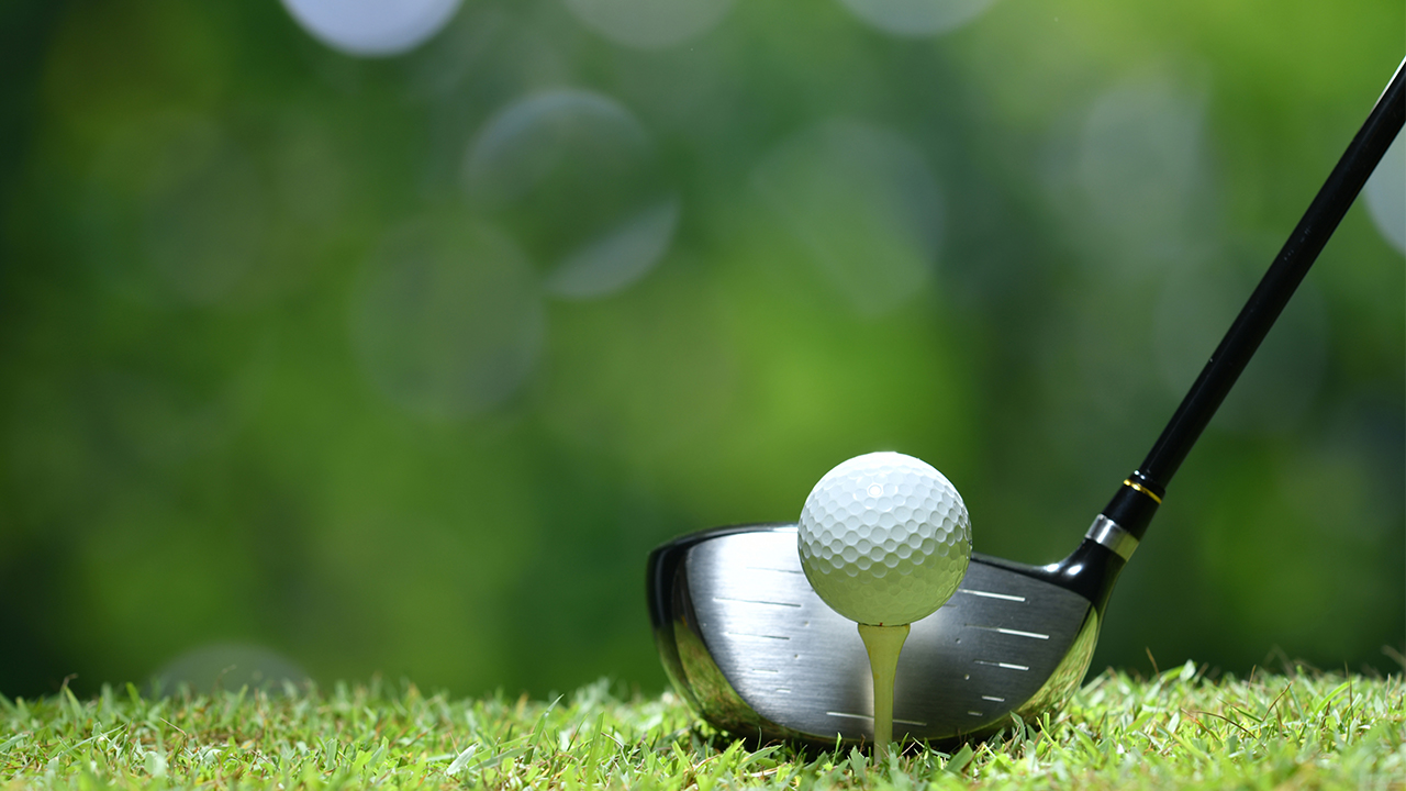 Balle de golf sur un té devant un bois de départ